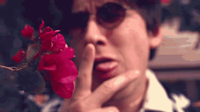 a close up of a person holding a red flower in front of their face