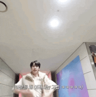 a man in a white vest is dancing in a hallway with korean writing on the wall