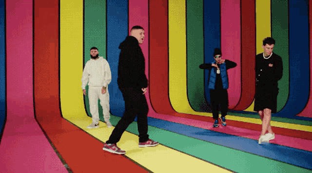 a group of men are dancing in front of a rainbow wall