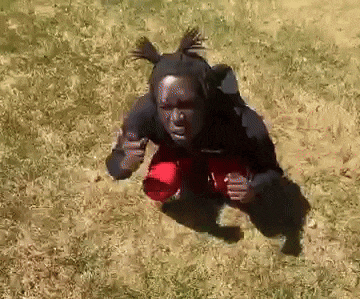 a person in a black shirt and red shorts is squatting on the grass