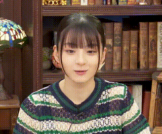 a young woman is standing in front of a bookshelf wearing a sweater .
