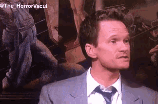 a man in a suit and tie is standing in front of a painting that says the horrorvacui on the bottom