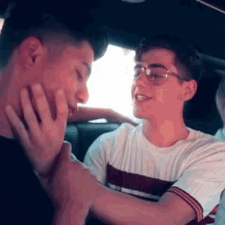 two young men are sitting in a car and one of them is holding the other 's hand .