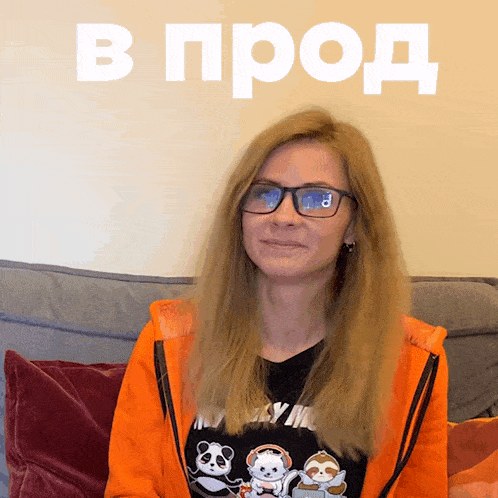 a woman wearing glasses and an orange jacket is sitting on a couch in front of a sign that says в прод