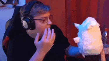a man wearing headphones and glasses is holding a stuffed animal in his hand .