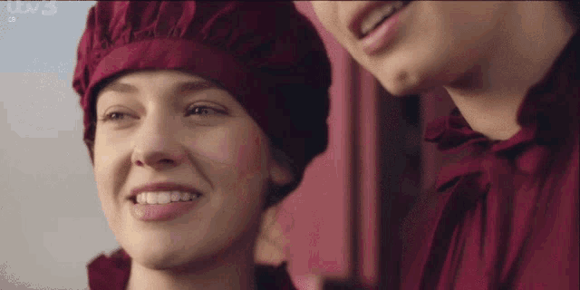 a woman wearing a red hat is smiling in front of a pink wall