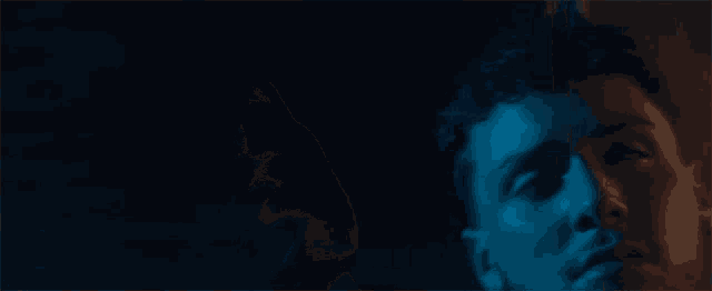 a close up of a man 's face in a dark room with blue light behind him .
