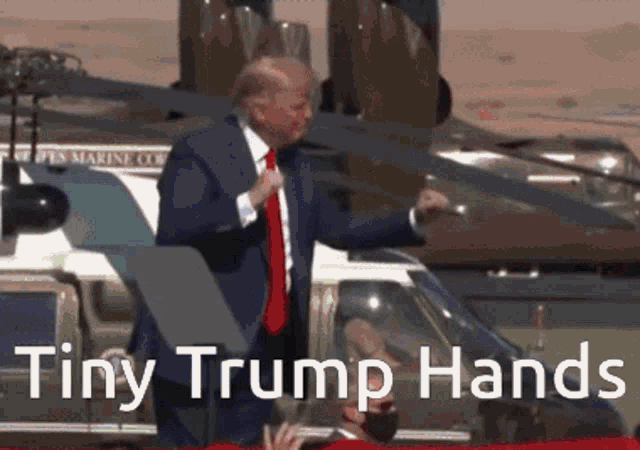 a man in a suit and tie stands in front of a helicopter with the words " tiny trump hands " above him