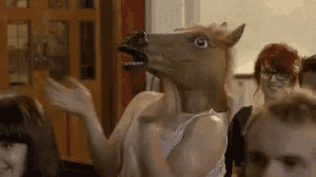 a woman wearing a horse mask is standing in front of a crowd of people .