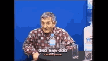 a man in a plaid shirt is sitting at a table with a bottle of water and a glass