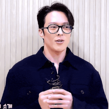 a man wearing glasses and a blue jacket is holding a microphone .