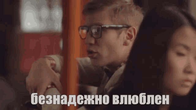 a man wearing glasses sits next to a woman on a bus and says " безнадежно влюблен "