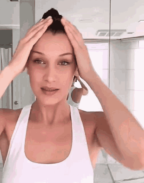 a woman in a white tank top holds her hair in a bun