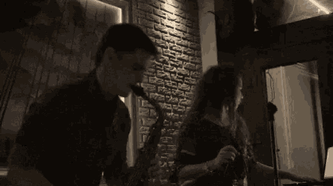a man playing a saxophone next to a woman playing a flute in front of a brick wall