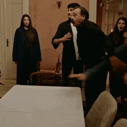 a group of people are standing around a table with a woman in a blue coat behind them
