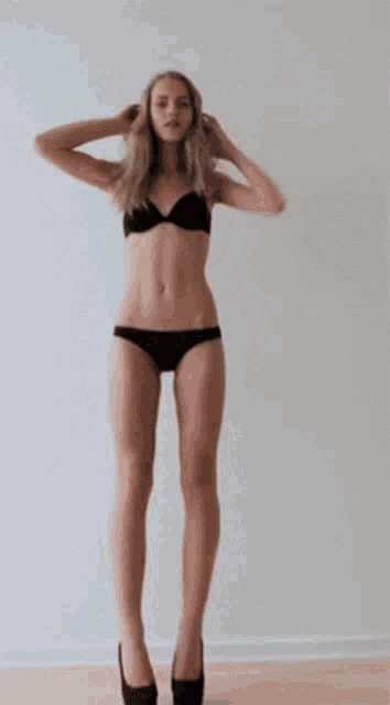 a woman in a black bikini and high heels is standing in front of a white wall .