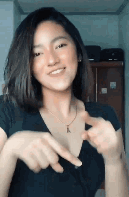 a young woman wearing a black shirt and a necklace is pointing at something .
