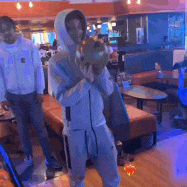 a man in a hoodie is holding a bowling ball in a restaurant .