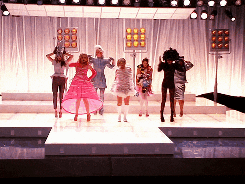 a woman in a pink dress stands on a runway with other models