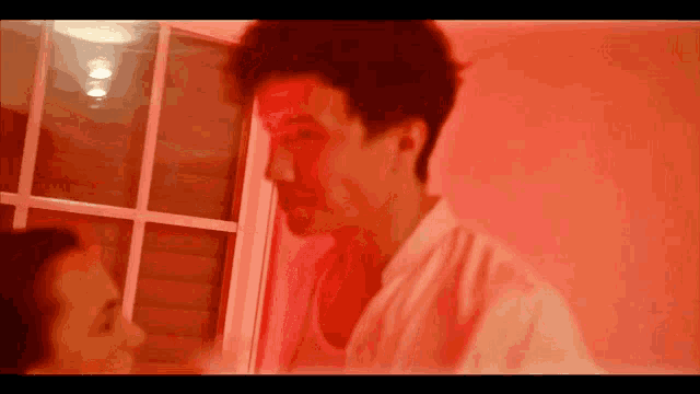a man and a woman are looking at each other in a room with red lights