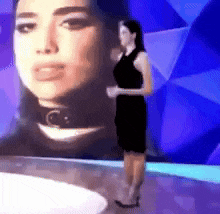 a woman in a black dress is standing in front of a large picture of a woman .