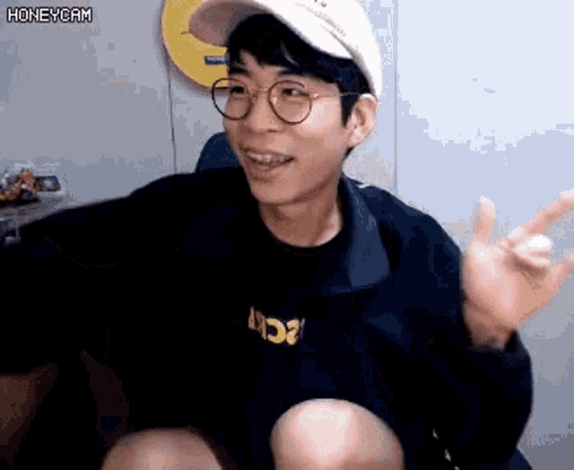 a young man wearing glasses and a hat is making a peace sign .