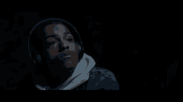 a young man wearing headphones and a hoodie is looking up in the dark .