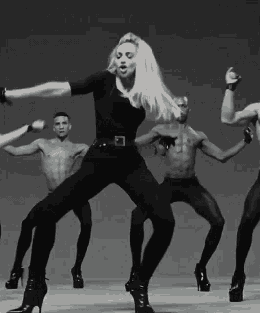 a woman in high heels is surrounded by men in tight pants