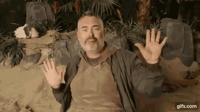 a man with a beard is laying in the sand and waving his hands .