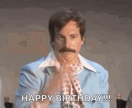 a man with a mustache is sitting at a table with his hands in his pockets and saying happy birthday .