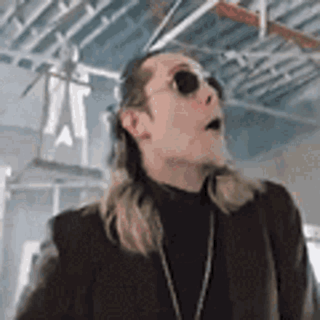 a man with long hair and sunglasses is wearing a black jacket and a turtleneck .