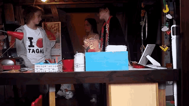 a girl wearing a shirt that says i tagao stands in front of a desk