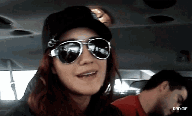 a woman wearing sunglasses and a hat is sitting in a car with rbd.gif written on the bottom
