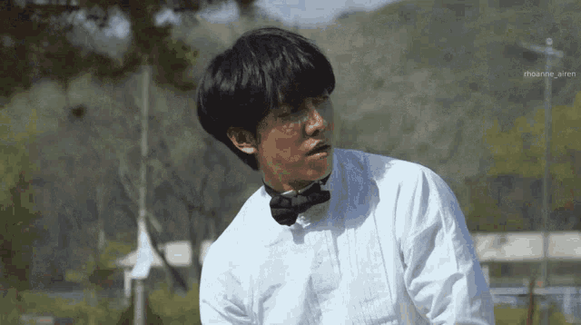 a man wearing a white shirt and a bow tie is standing in a park .
