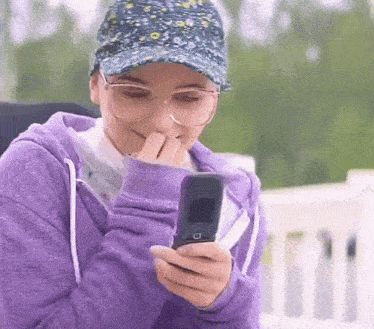 a woman wearing glasses and a hat is holding a flip phone .
