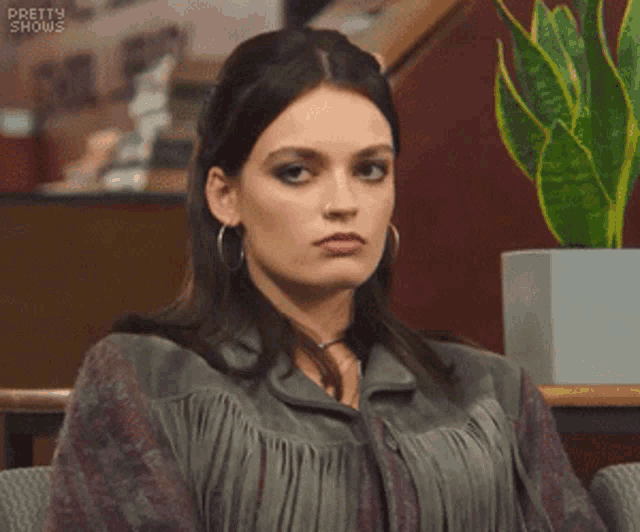 a woman is sitting in a chair with a plant in the background and making a funny face .