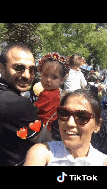 a woman wearing sunglasses holds a baby in her arms while a man looks on