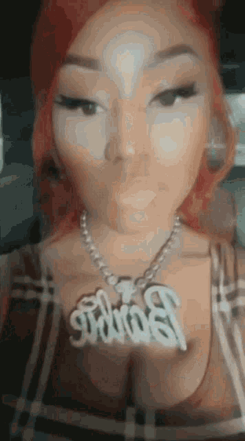 a woman with red hair is wearing a plaid shirt and a necklace that says dumb .