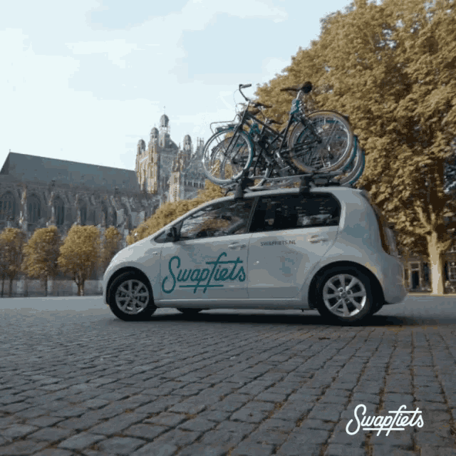 a white swapfiets car with bikes on top of it