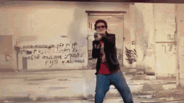 a man holding a gun in front of a wall that has graffiti on it