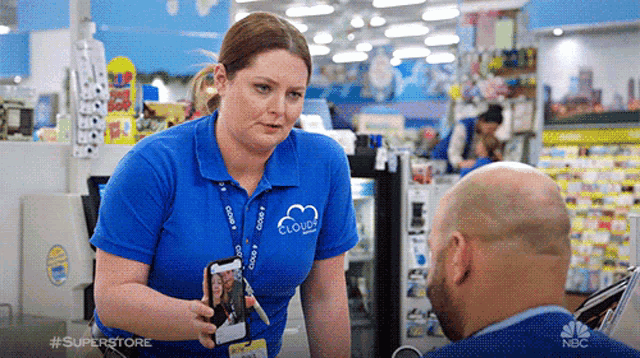 a woman in a blue shirt with the word cloud on it is talking to a bald man .