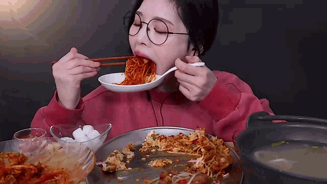 a woman wearing glasses is eating noodles with chopsticks .