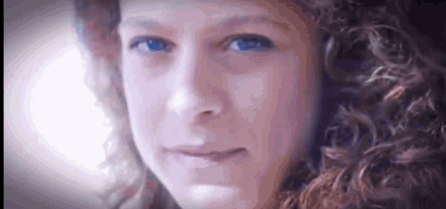 a close up of a woman 's face with curly hair and blue eyes looking at the camera .