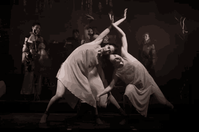 two women are dancing in a dark room with a man in a red hat behind them