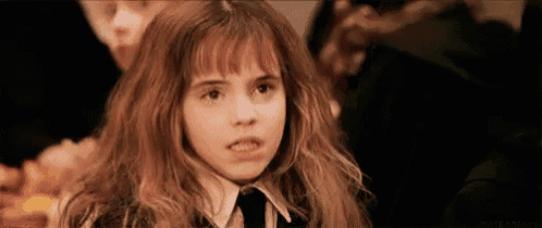 a young girl with long hair and bangs is making a funny face while sitting at a table .