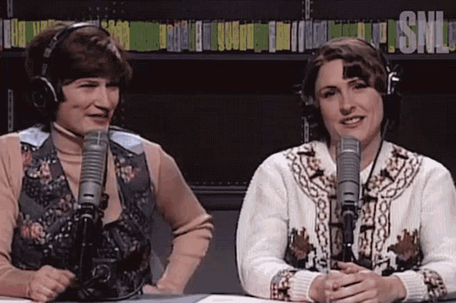 two women wearing headphones are sitting in front of microphones and the word snl is on the shelf behind them