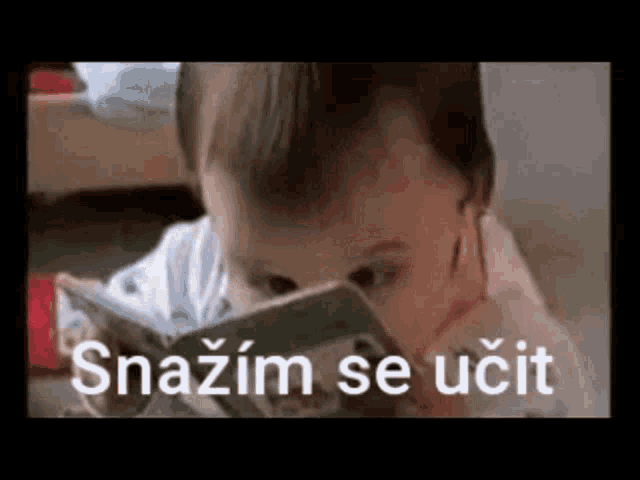 a baby is reading a book with the words snazim se učit on the bottom of the screen .