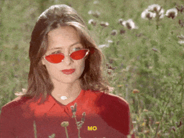 a woman wearing red sunglasses is standing in a field of flowers and the word mo is on the bottom