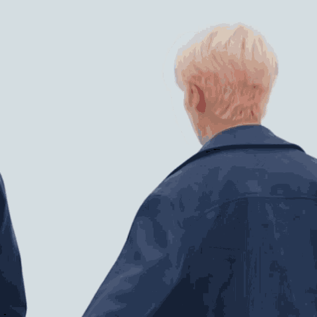 a man with blonde hair is wearing a blue jacket and looking at something .