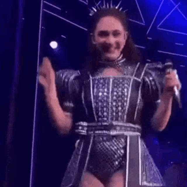 a woman in a costume is standing on a stage holding a microphone and clapping .